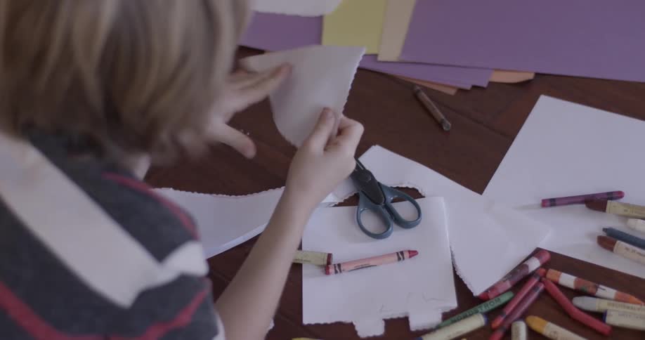 A child cuts paper on a table with jagged scissors to create different shapes on the paper after unfolding
