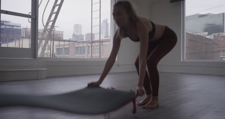 A woman unfurls a yoga mat on a wooden floor and flattens it on her hands and knees