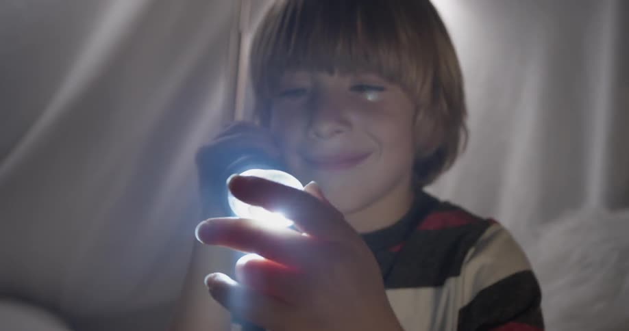 A boy shines a flashlight through a glass rock inside a fort he made