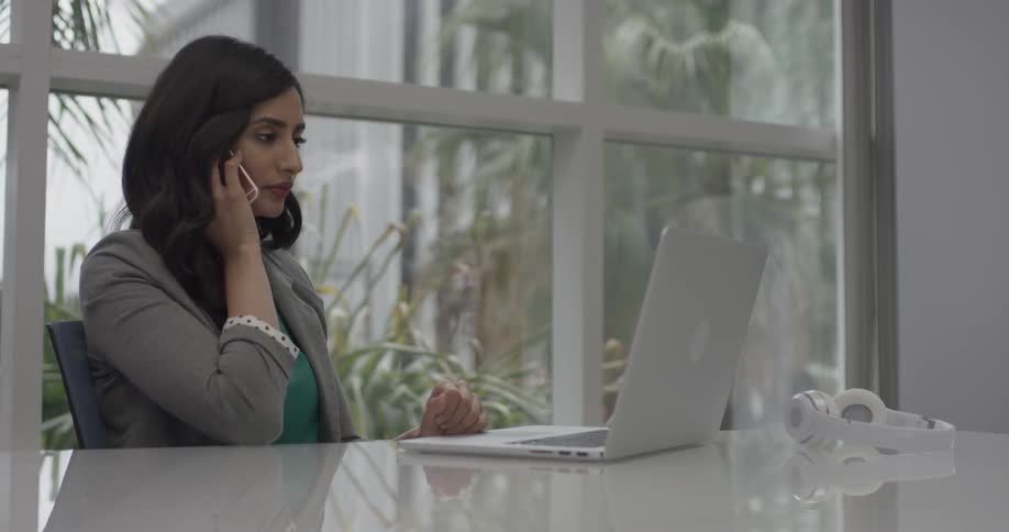 A woman talking on a phone while using a laptop in the office