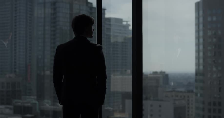 Man's silhouette at a window of a tall building looking at other skyscrapers