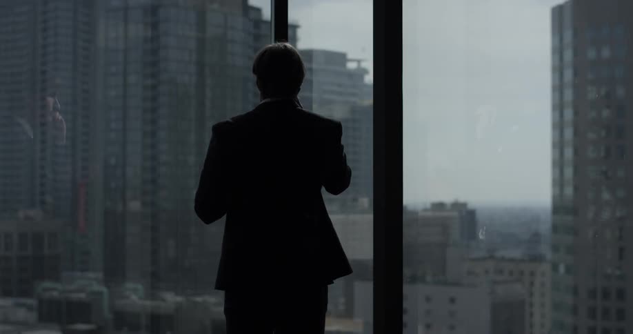 A man is talking on the phone while looking outside at the city view of buildings