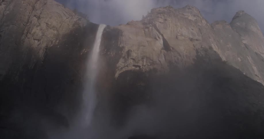 A waterfall has water falling off of a tall mountain and is creating fog below which raises the humidity and covers the lens a bit