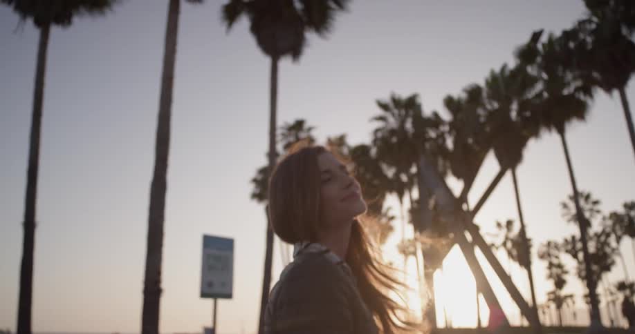 Woman smiles and turns around on the beach near palm trees