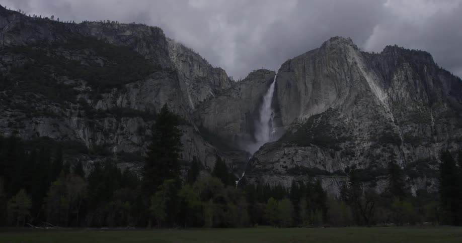 A waterfall crashes to the bottom of a cliff that has a line of trees at its base