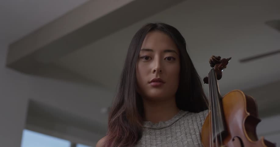 A woman looking down and holding a violin
