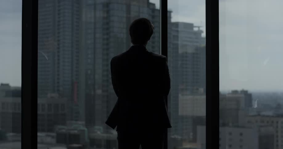 A business man looks out his window over the city