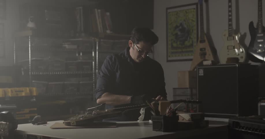 A man uses a cloth to polish an electric guitar in a dark garage
