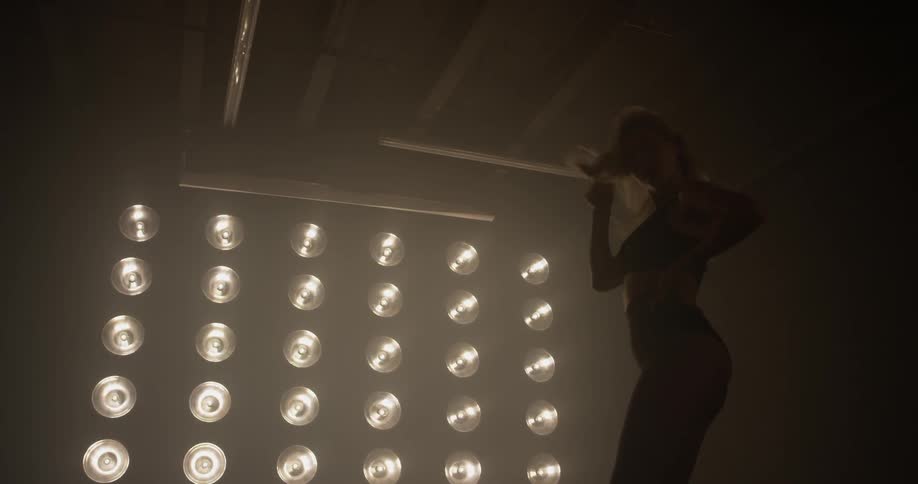 A woman twirling her hair and dancing in front of large lights