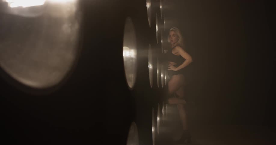 Women of fake blond hair dances sexy and strikes sensual poses in front of a bunch of lights on the wall in a dark room with underwear on