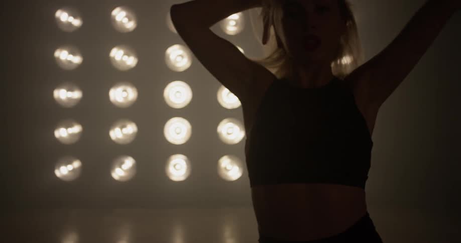 A woman dances in front of bright spot lights