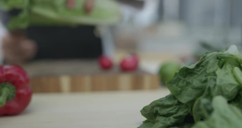 A chef grabs some lettuce in front of them and begins to chop it up on the cutting board