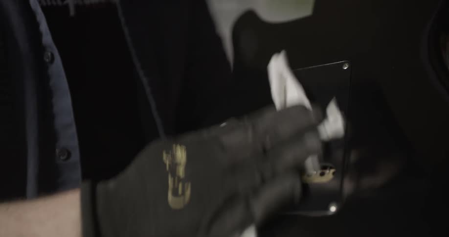 A gloved hand polishes the back of a guitar