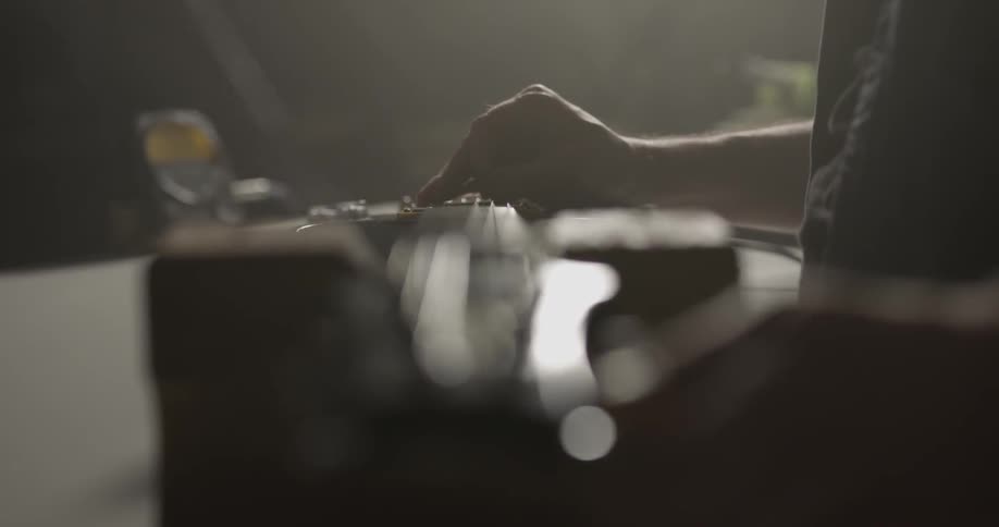 Person winds guitar strings with guitar laying on table