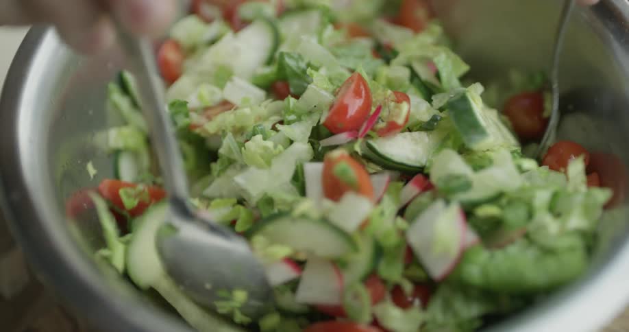 Someone is mixing a salad in a bowl