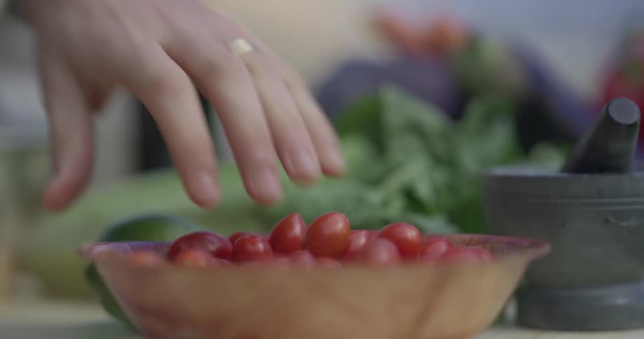A chef grabs a handful of tomatoes out of a bowl on the table