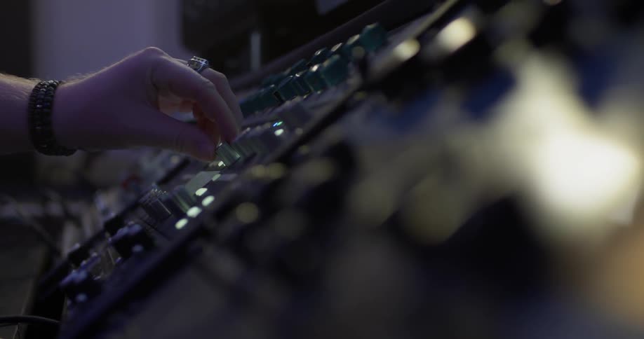 A human hand with a wedding ring and wrist watch grabs a knob on the sound mixing electronic board equipment and turns it to the left