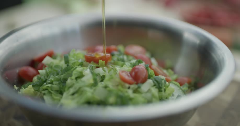 Lettuce tomatoes and olive oil are put in a metallic bowl on a table