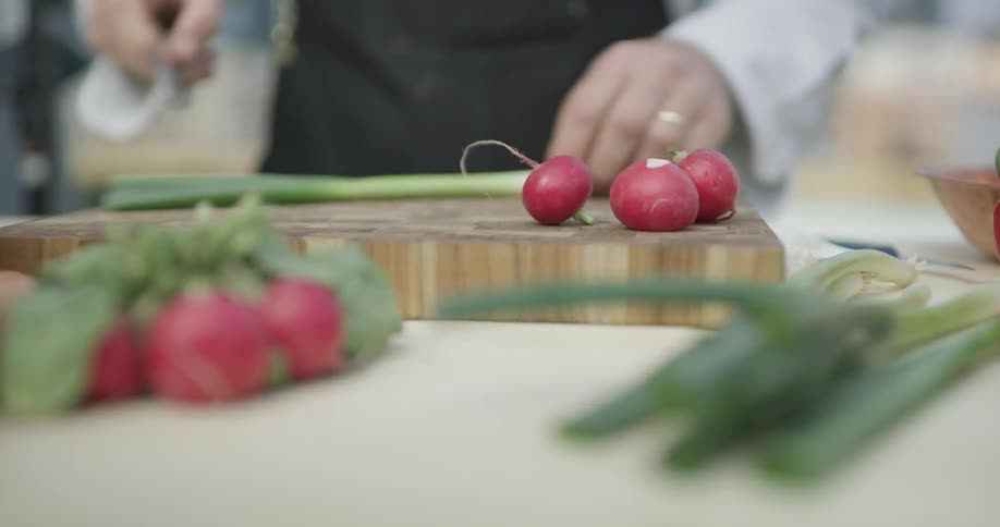 A man is chopping up chives on a cutting board outside on a sunny day with a sharp knife