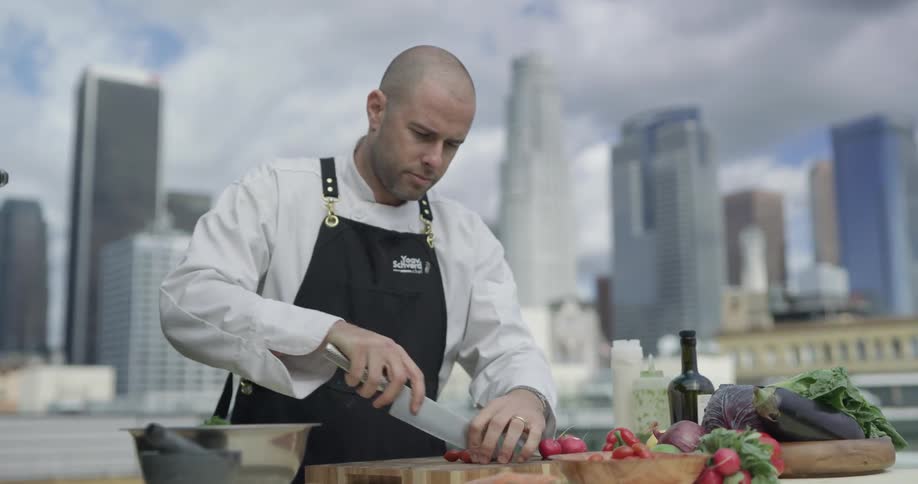 A chef cuts small tomatoes on a cutting board on a rooftop in a city