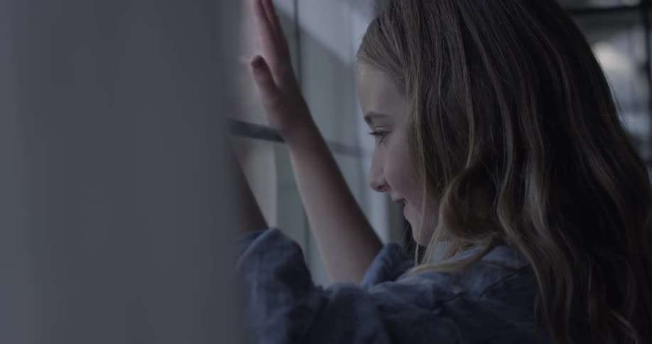 A girl presses her hands repeatedly against a window