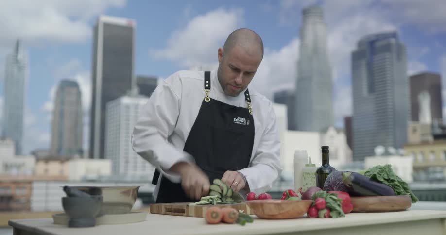 Chopping cucumbers on a cutting board outside on top of a building with a city skyline on a sunny day