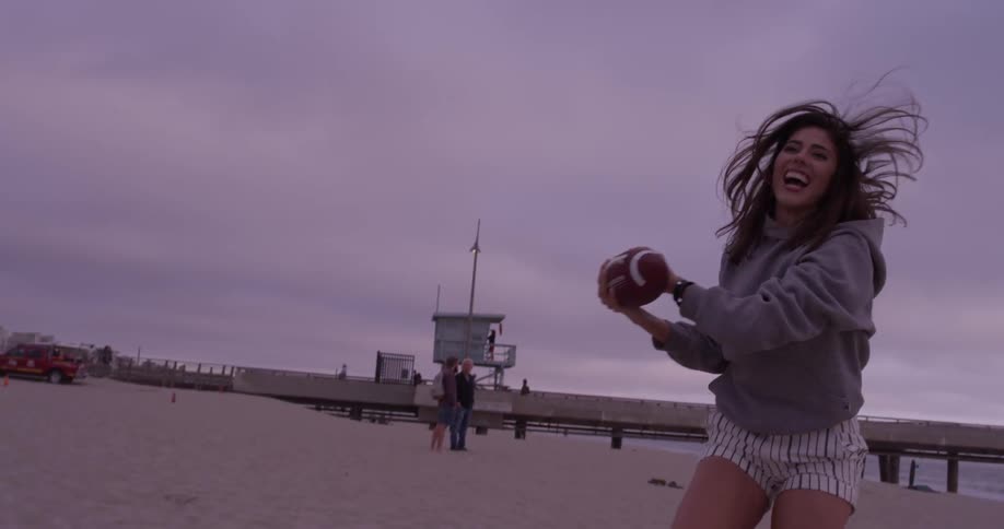 A woman is catching a football outside on the beach