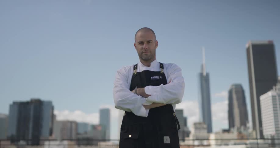 Man wearing an apron stands resolutely with a cityscape as a backdrop