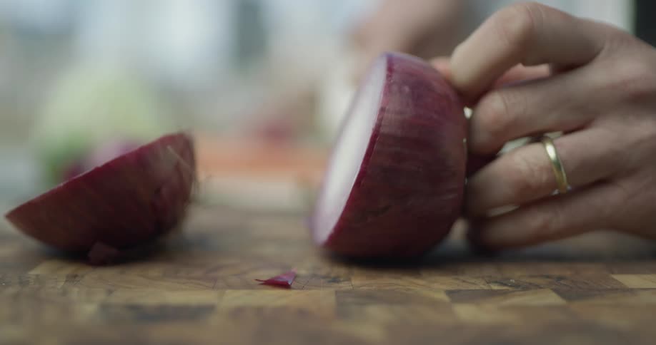 Someone uses a large knife to cut an onion