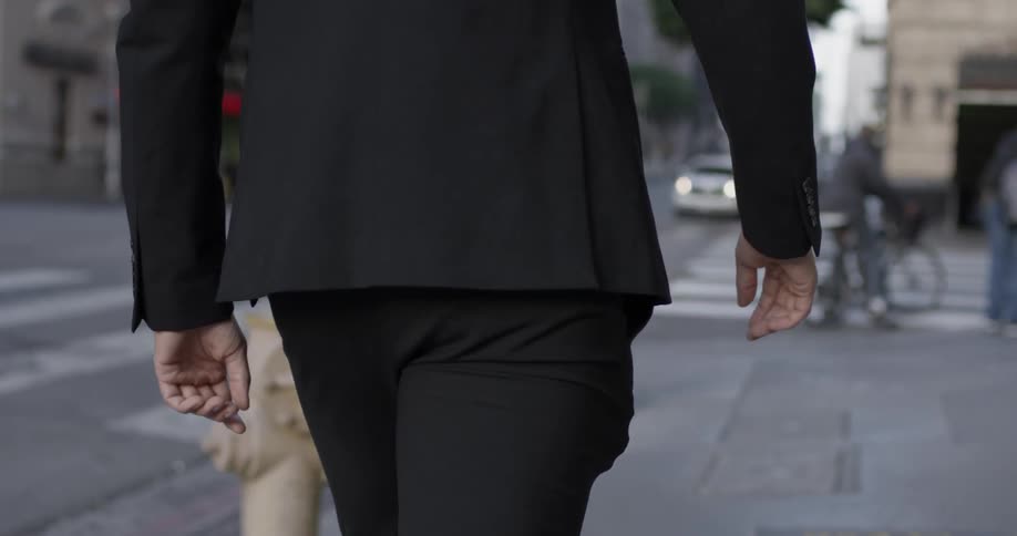 A man walks forwards on a sidewalk of a busy street in a downtown part of a large city while wearing a suit and nice shoes
