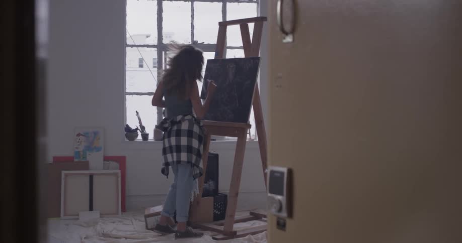 Woman paints on canvas in brightly lit room