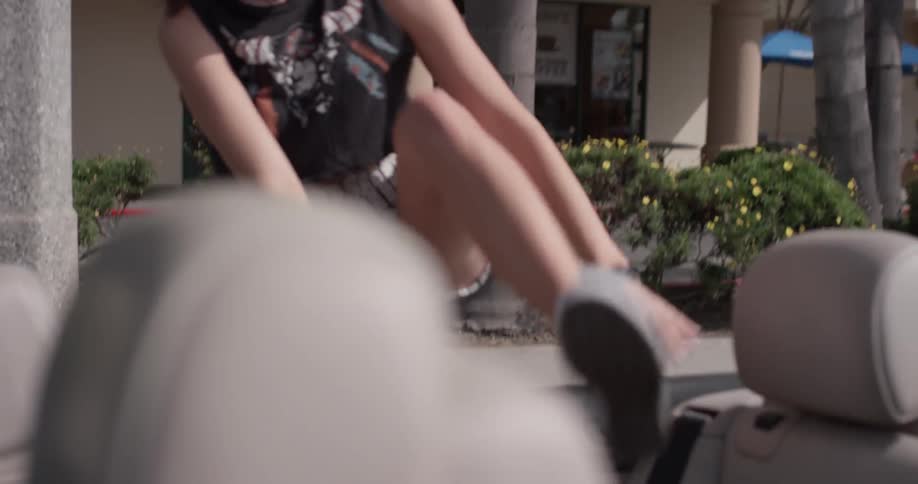 A woman climbs over the door of a convertible