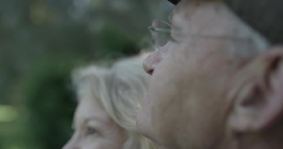 Older male sitting next to older female looks around at noon