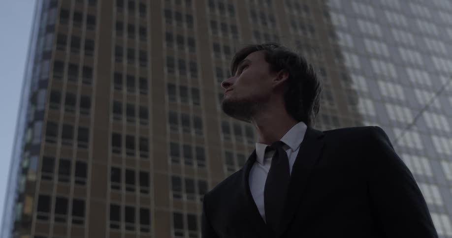 Young man in a suit looking up at the tall building in the city