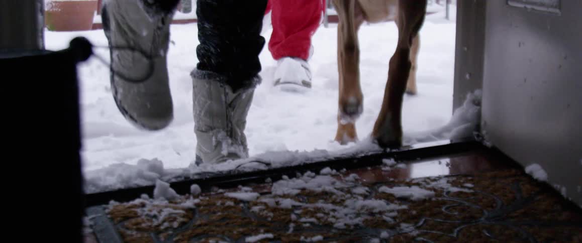People with boots walking through snow as they approach a doorway