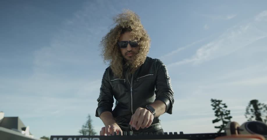 A man with long curly hair plays a keyboard under the blue sky
