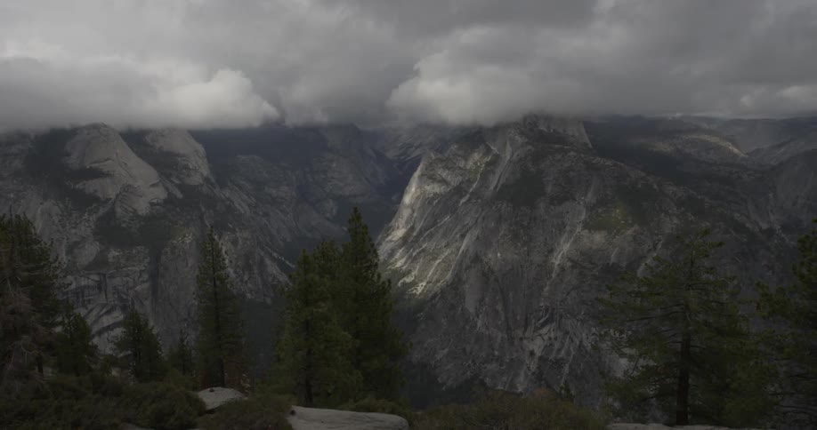 Fluffy gray clouds move across the tops of huge cliffs
