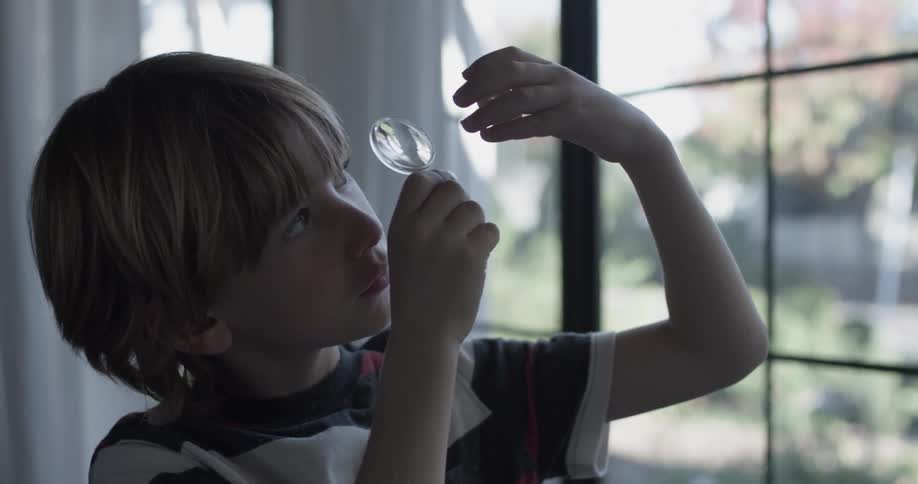 A boy looks at a glass oval through a magnifying glass made of plastic