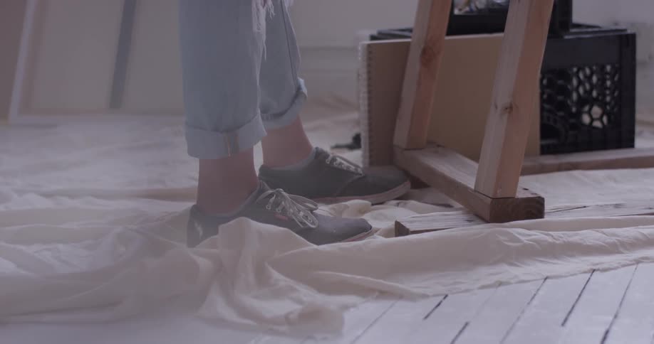 A person's feet wearing tennis shoes stand on a drop cloth on a white wood floor