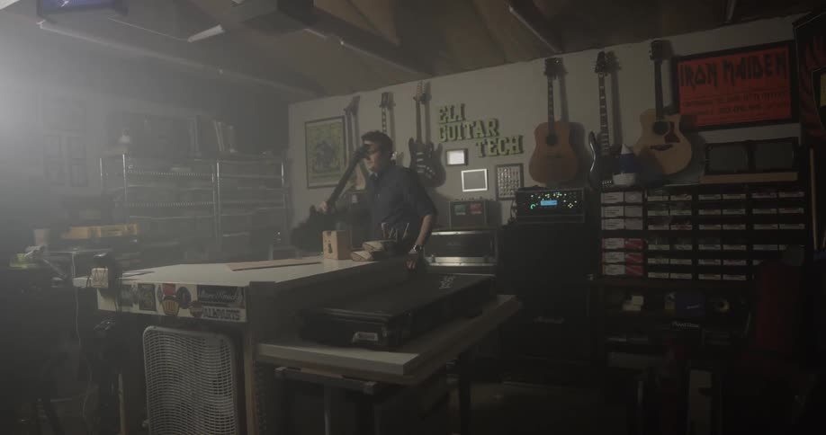 A man gets a guitar out of its case then brings it around a table then sets it down