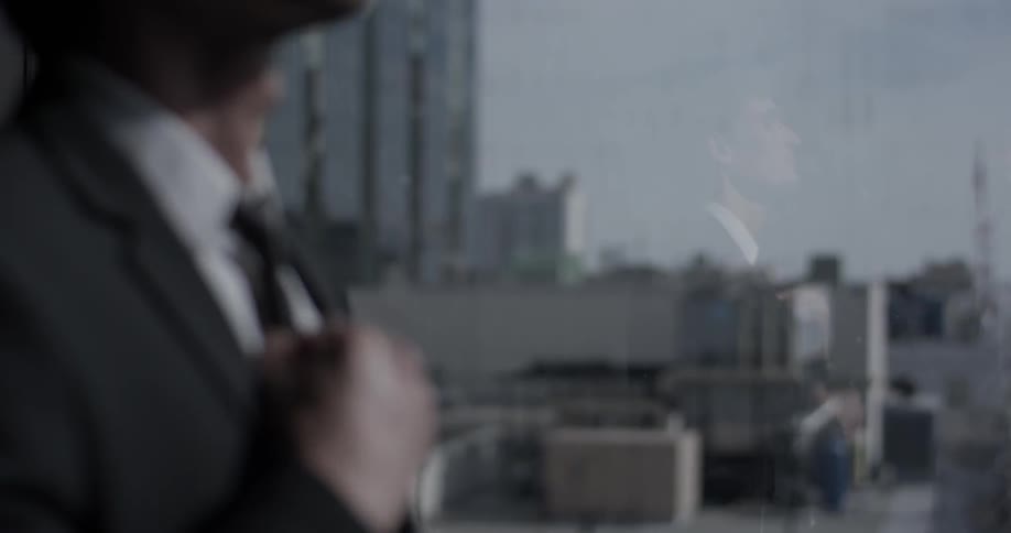 A man in a suit straightens his tie as he looks out at the city