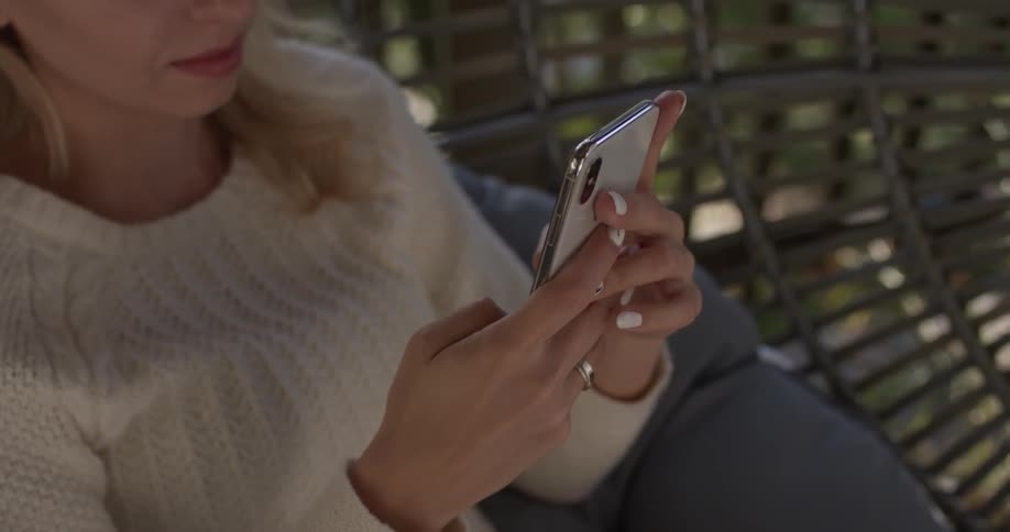 Woman sits on a metal swing typing on a phone