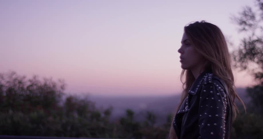 Woman walks outside past trees at sunset