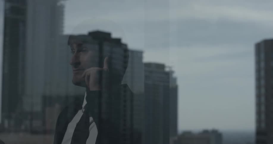 A man can be seen through a window which is reflecting the city skyline he is looking out at