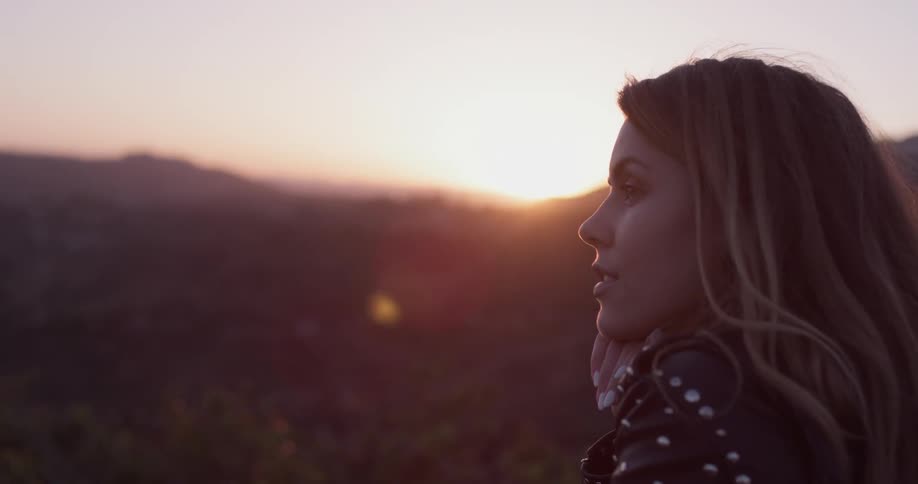Woman stands outside at sunrise looking out