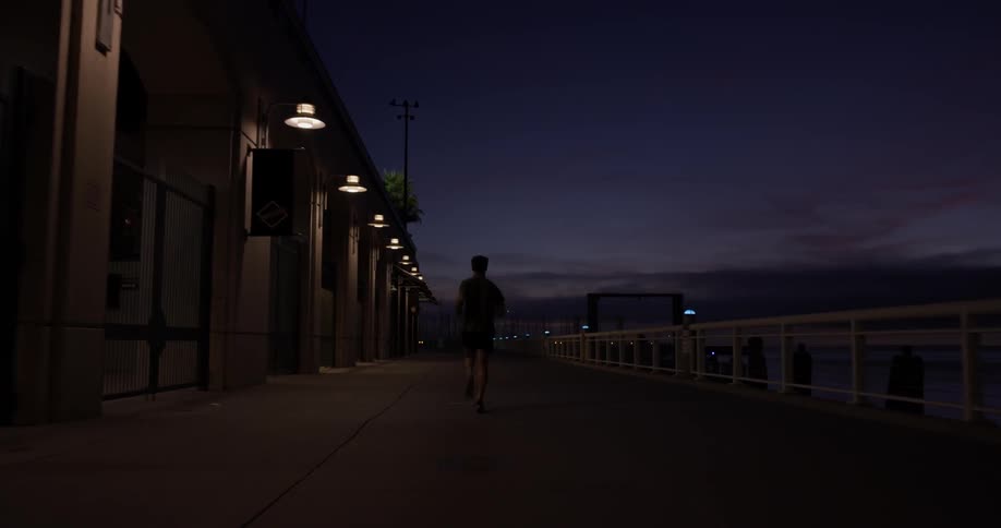 A man runs along a path lit by evenly spaced lights until he reaches the end and plunges on into the dark