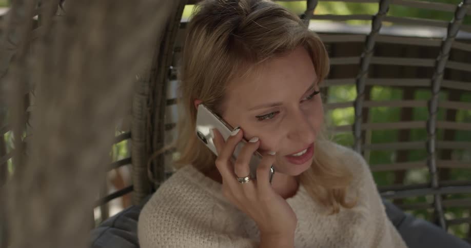 A woman sits on a wicker chair talking on a cell phone