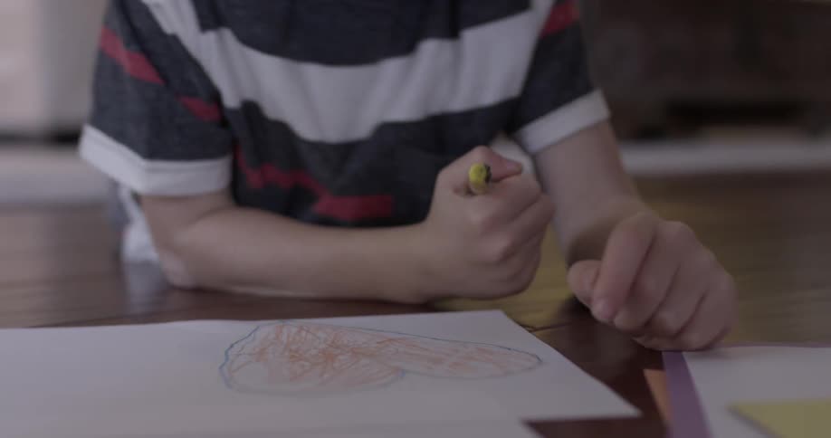 A child lays on the floor holding a crayon and drawing on a sheet of paper