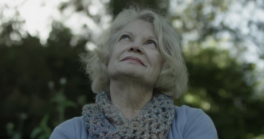 A woman looks at the sky discontentedly but then begins to smile as the camera operates in slow motion