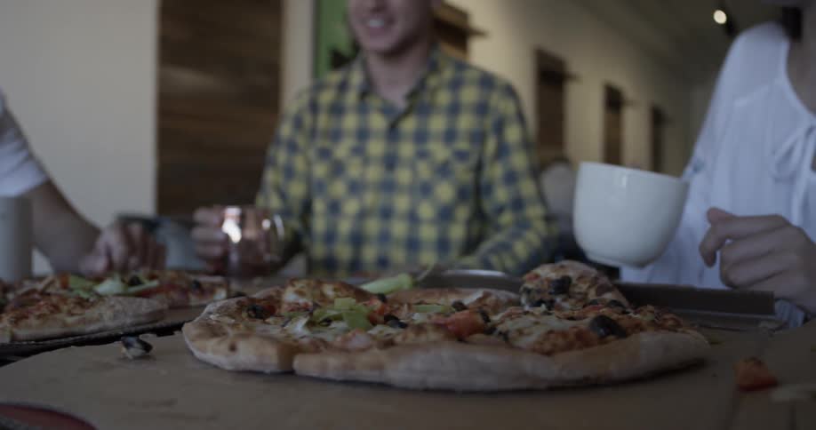 Multiple people sitting around a table of pizzas